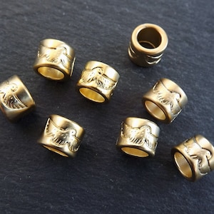 May include: Eight gold-colored metal beads with a raised design of a bird with wings spread. The beads are approximately 1 cm in diameter.