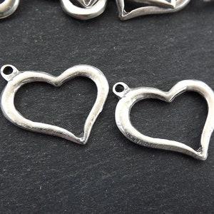 Op de afbeelding: Twee zilveren open hartbedels met een lus aan de bovenkant om aan sieraden of knutselwerk te bevestigen.