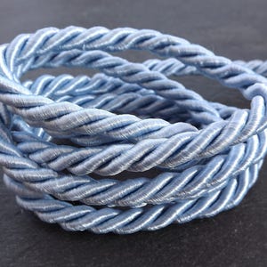 May include: A close-up of a light blue braided cord. The cord is made of a soft, silky material and is perfect for adding a touch of elegance to any project.