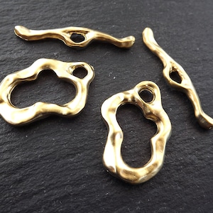 Könnte beinhalten: Vier goldfarbene Metall-Anhänger mit abstrakter, organischer Form. Die Anhänger haben ein Loch zum Anbringen an Schmuck oder anderen Bastelarbeiten.