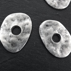 May include: Two silver metal oval-shaped charms with a hole in the center. The charms have a textured surface.