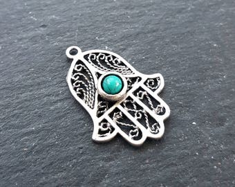 May include: Silver charm in the shape of a hamsa hand with a turquoise stone in the center.