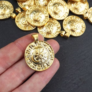 Pode incluir: Um close-up de um pingente de metal dourado com um design de sol e lua. O pingente &eacute; intrincadamente detalhado e tem uma forma circular. Ele &eacute; cercado por outros pingentes semelhantes.