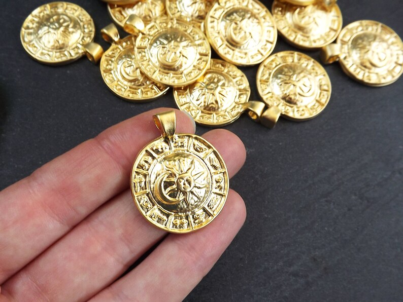 Pode incluir: Um close-up de um pingente de metal dourado com um design de sol e lua. O pingente &eacute; intrincadamente detalhado e tem uma forma circular. Ele &eacute; cercado por outros pingentes semelhantes.