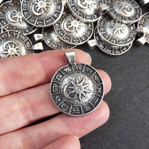 May include: Silver pendant with a circular design featuring a sun and moon symbol surrounded by zodiac signs.