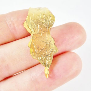 Puede incluir: Pendiente de metal dorado con un dise&ntilde;o intrincado y un bucle en la parte inferior para sujetar una cadena.