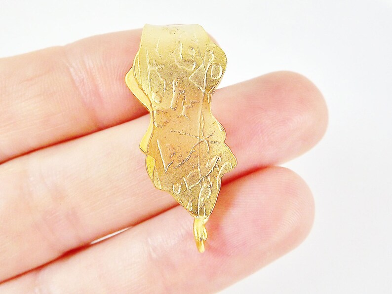 Puede incluir: Pendiente de metal dorado con un dise&ntilde;o intrincado y un bucle en la parte inferior para sujetar una cadena.