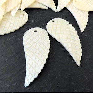 May include: A set of white, carved, shell angel wings with a diamond pattern. The wings have a hole at the top for hanging or attaching.