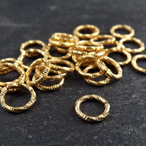 May include: A pile of gold-colored metal jump rings. The rings are all the same size and have a textured surface.