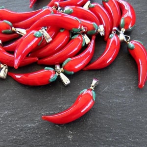 Puede incluir: Un montón de abalorios de chile rojo de vidrio con cierres plateados y tapas verdes.