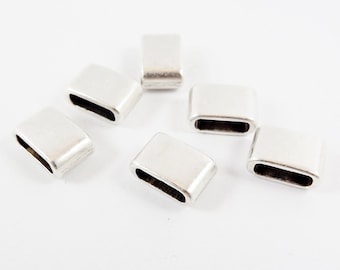 Könnte beinhalten: Sechs silberfarbene, rechteckige Schmuckelemente mit abgerundeten Kanten liegen auf einer weißen Oberfläche. Jedes Element hat eine hohle, oval geformte Öffnung. Die Elemente scheinen aus Metall zu sein.