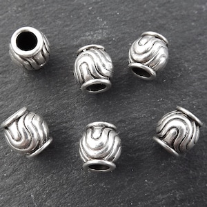 Könnte beinhalten: Sechs silberne Metallperlen mit einem wellenförmigen Design. Die Perlen haben ein Loch in der Mitte zum Aufziehen.