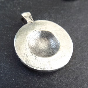 May include: Silver pendant with a round, slightly concave front. The pendant has a smooth, polished surface.
