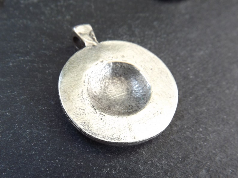 May include: Silver pendant with a round, slightly concave front. The pendant has a smooth, polished surface.