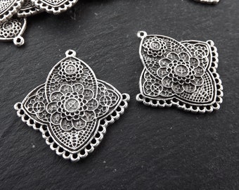 May include: Two silver filigree pendant charms with a floral design. The charms have a square shape with rounded corners and a loop at the top for attaching to a necklace or bracelet.