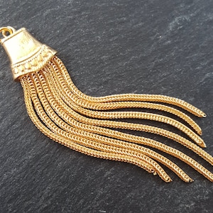 May include: Gold tassel pendant featuring a chain design. The tassel is made up of multiple strands of chain linked together at the top. The pendant measures approximately 5 cm in length.