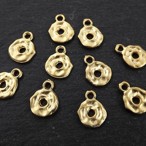 Pode incluir: Dez pingentes de metal dourado com acabamento texturizado martelado. Cada pingente apresenta um círculo redondo aberto no centro e um pequeno laço na parte superior para prender em joias ou outros artesanatos.