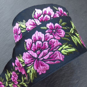 Puede incluir: Cinta negra con flores bordadas en rosa y verde. La cinta está doblada por la mitad y las flores son visibles en ambos lados.