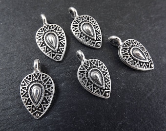 May include: Five silver-toned metal charms in the shape of a teardrop with intricate geometric designs. Each charm has a loop at the top for attaching to jewelry or other crafts.