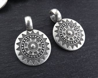 May include: Two silver-toned metal charms in the shape of a sun with intricate geometric designs. The charms have a loop at the top for attaching to a necklace or bracelet.