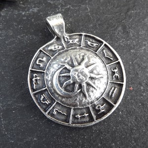 May include: Silver pendant featuring a circular design with a sun and moon in the center, surrounded by zodiac symbols.