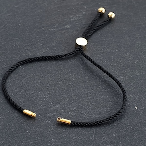 May include: A black adjustable cord bracelet with gold-toned metal accents. The bracelet has a sliding knot closure.