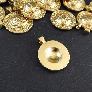 Pode incluir: Um grupo de pingentes de metal dourado com um design circular. Os pingentes t&ecirc;m um centro elevado e uma superf&iacute;cie texturizada. Um pingente est&aacute; deitado de costas, mostrando o interior liso e c&ocirc;ncavo.
