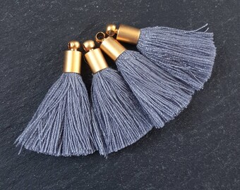 May include: Four gray tassel trim with gold metal caps. The tassels are made of soft, fluffy fibers.