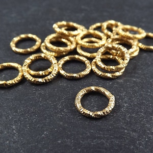 Könnte beinhalten: Ein Haufen goldfarbener Sprungringe mit einer strukturierten Oberfläche. Die Sprungringe sind in einem zufälligen Muster angeordnet.