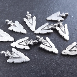 May include: A collection of ten silver arrowhead charms. The arrowheads are all the same size and shape, and they have a slightly textured surface.