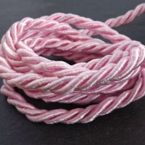 Puede incluir: Cordón trenzado rosa, una cuerda suave y delicada con un acabado satinado. Este cordón es perfecto para manualidades, decoración o para agregar un toque de elegancia a cualquier proyecto.