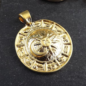 Pode incluir: Pingente dourado com um design circular, um sol e uma lua no centro e s&iacute;mbolos do zod&iacute;aco ao redor da borda.