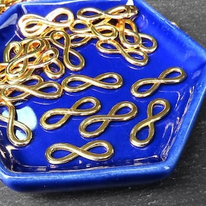 May include: A blue hexagonal dish filled with gold infinity symbol charms. The charms are scattered randomly on the dish.