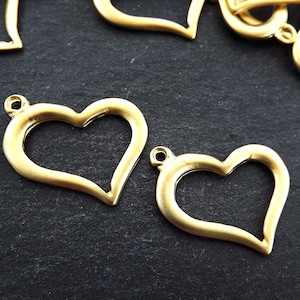 Könnte beinhalten: Zwei goldfarbene Metall-Anhänger in Herzform mit einer Öse oben zum Anbringen an Schmuck oder andere Bastelarbeiten.