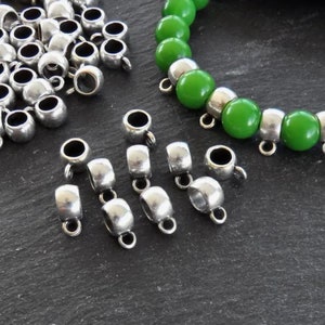 May include: Silver metal bead caps with a loop on top. The caps are scattered on a dark gray surface. A green beaded bracelet is also shown in the image.