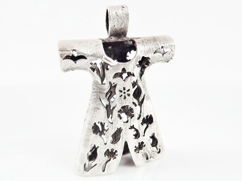 Pu&ograve; includere: Ciondolo color argento con un design floreale. Il ciondolo presenta un design traforato stilizzato di fiori e foglie. L'anello &egrave; un semplice anello. Il ciondolo &egrave; su sfondo bianco.