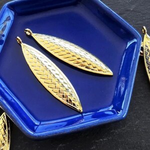 May include: Gold leaf-shaped metal charms with a woven pattern. The charms have a loop at the top for attaching to jewelry or other crafts.