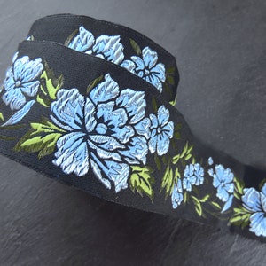 Puede incluir: Cinta negra con un diseño floral con flores bordadas en azul y verde.