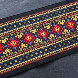 Peut inclure: Tissu noir avec un motif brodé coloré. Le motif présente des formes géométriques en rouge, jaune, bleu et or. Le tissu a une texture tissée.