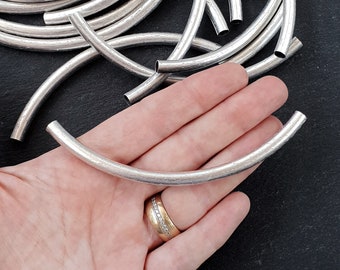May include: A close-up of a silver metal tube bead. The bead is about 1 inch in diameter and has a smooth, slightly textured surface. The bead is held in a hand, showing its size and shape.