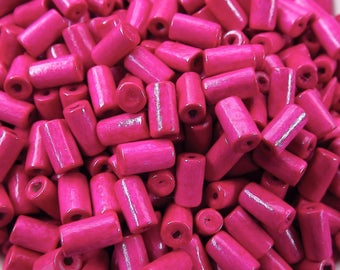 Puede incluir: Primer plano de un montón de cuentas de madera de color rosa brillante. Las cuentas son de forma cilíndrica y tienen un acabado liso y brillante.