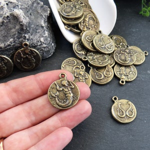May include: A collection of antique gold-toned metal charms featuring a mermaid design. The charms are round and have a detailed design of a mermaid with flowing hair and a tail.