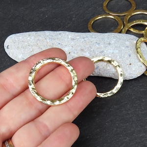 May include: Gold-toned metal jump rings with a hammered texture. The rings are approximately 1 inch in diameter.