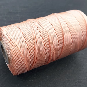 May include: A spool of peach-colored cord, wound tightly and ready for crafting projects.