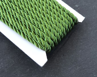 May include: A spool of green twisted cord, the cord is on a white card, the card is on a black surface.