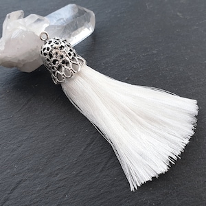 Peut inclure: Un pompon blanc avec un capuchon en métal argenté. Le pompon est fait de fibres douces et blanches et présente un design délicat et complexe.