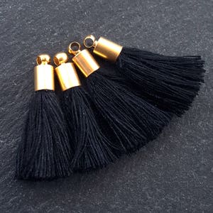 May include: Four black tassel trims with gold metal tops. The tassels are arranged in a fan shape.