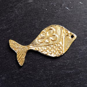 Può includere: Un ciondolo a forma di pesce in metallo dorato con un design dettagliato. Il pesce ha un motivo floreale sul corpo e una coda testurizzata.