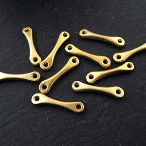 May include: A group of 10 gold-colored metal connector charms with a curved shape. The charms are scattered on a black surface.