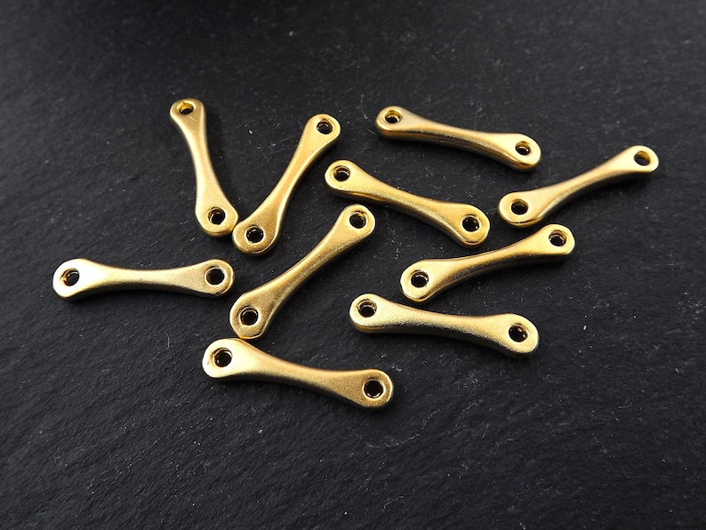 May include: A group of 10 gold-colored metal connector charms with a curved shape. The charms are scattered on a black surface.